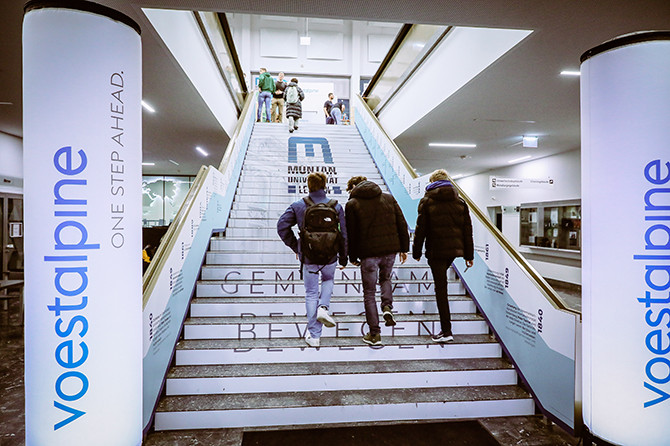 The staircase in the entrance area of Montanuniversität Leoben with a voestalpine display signposting the way to the event.