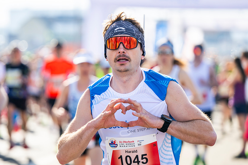 Einen Nahaufnahme eines Teilnehmers beim voestalpine cares run. Während er läuft, formt er mit seinen Fingern ein Herz vor seiner Brust.