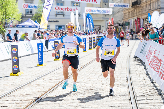 Zwei Teilnehmer laufen beim voestalpine cares run in Richtung Kamera. Die Beiden strahlen und haben sichtlich Spaß.