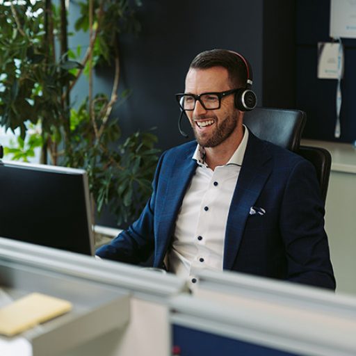 Justin sitzt mit Headset an seinem Schreibtisch mit Blick auf den Computer Bildschirm.