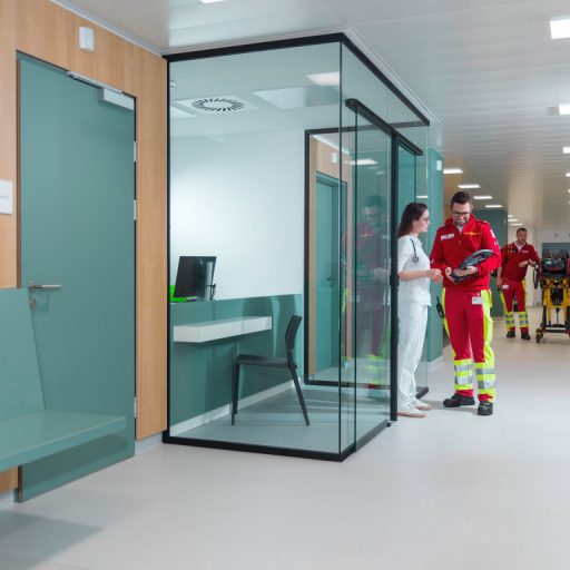 Medical staff in a medical facility. In the background are two paramedics with medical equipment. A paramedic and a doctor are talking in front of them. The paramedic holds a tablet in his hand and shows the doctor something on it.