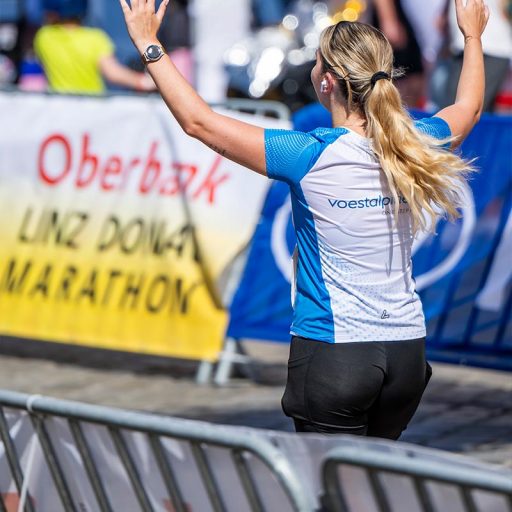 voestalpine employee runs through the finish line of the Linz Marathon with her arms raised
