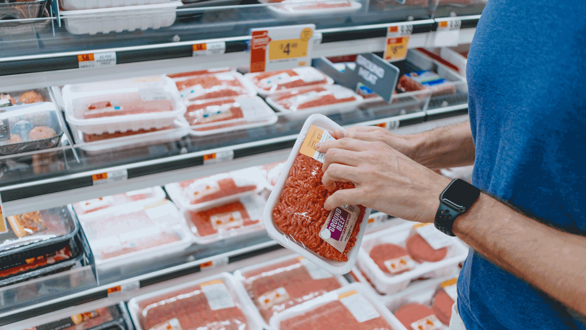 a man holding up a packet of gground beef at the supermarket