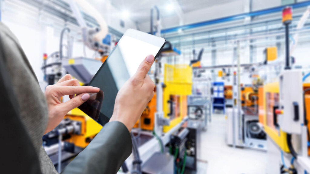 macchina per stampaggio a iniezione di plastica in un sito di produzione e un lavoratore con un tablet che scorre con le dita